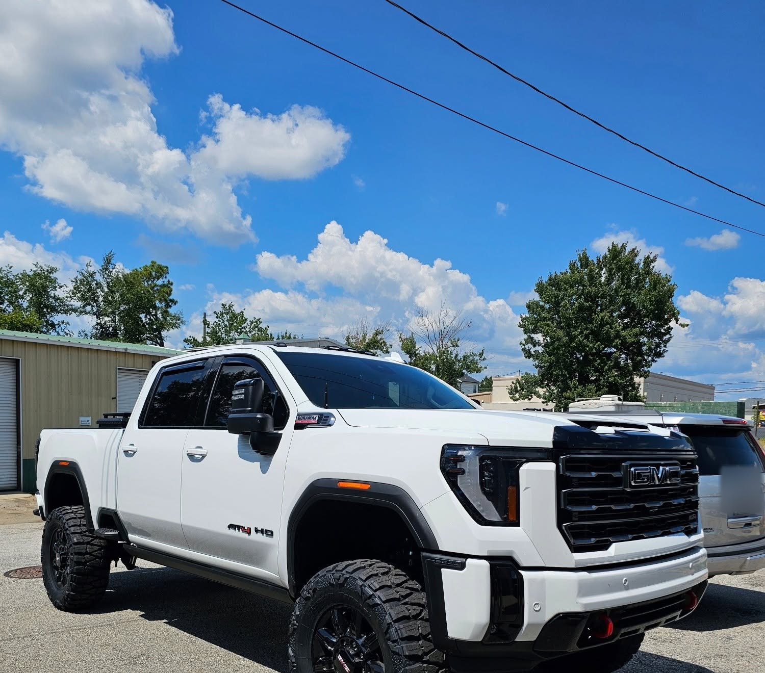 White GMC 2500 AT4 HD with a lift and black wheels at Automotive Highlights